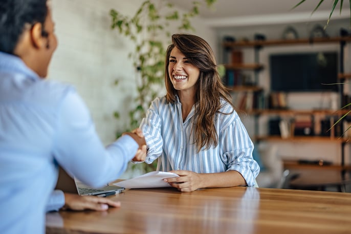 A smiling woman shaking hands during a job interview in an office.