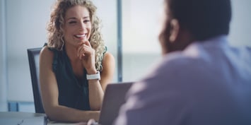 A curly haired woman smiles at a potential employee during an interview 