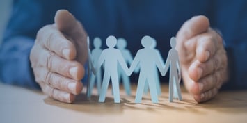 A hand protects paper dolls symbolising a company's workforce.