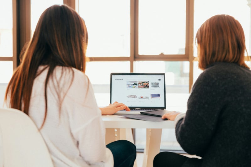 Two women facing a laptop