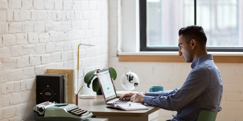 A man sits at a computer at work, typing on on the keyboard