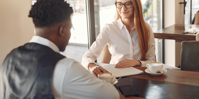 A man and woman seated at a desk across from each other. Both are dressed in professional attire and appear to be engaging in a job interview. A man and woman seated at a desk across from each other. Both are dressed in professional attire and appear to be engaging in a job interview.