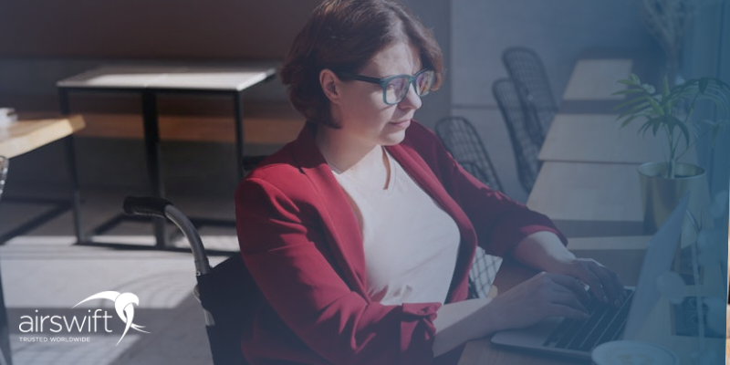A woman in a wheelchair wearing a red blazer thoughtfully looks at a laptop, on which she is applying for a job 