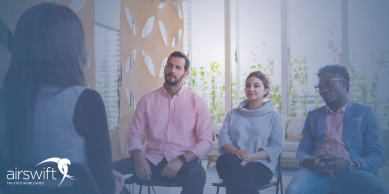 A group interview led by a woman, she is speaking to three smartly dressed individuals in a light and airy office environment