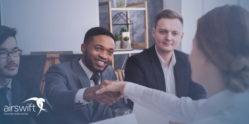 A woman in a white shirt shakes hands with a man in a suit, in a formal office setting. The atmosphere is relaxed