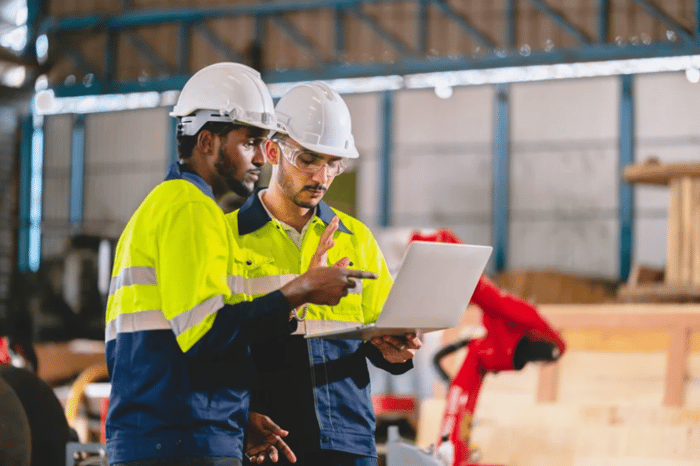 Two male engineers wearing hi-vis' and white hardhats reading off a laptop